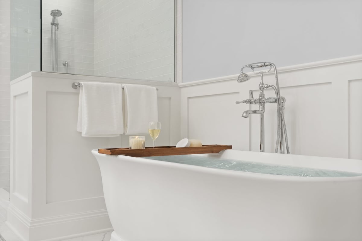 Freestanding soaking tub with water and a wooden bath tray in a Shaker Heights bathroom by Chagrin River Company.-optimized