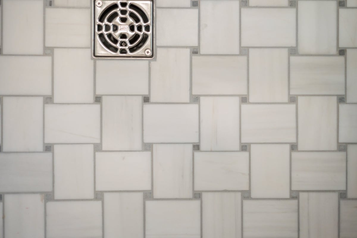 White woven-pattern shower floor tile with metal drain in a Shaker Heights bathroom by Chagrin River Company.-optimized
